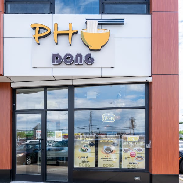 The exterior of Pho Dong restaurant, featuring its sign, large windows, and menu posters.