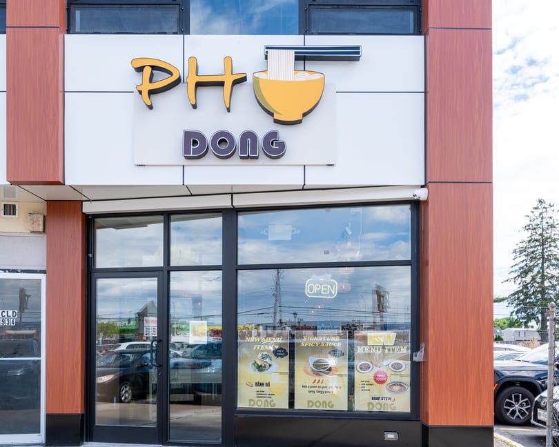 The exterior of Pho Dong restaurant, featuring its sign, large windows, and menu posters.