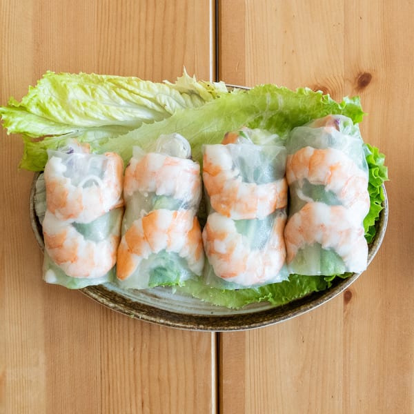 Four fresh shrimp spring rolls on a bed of lettuce, with a side of peanut sauce.