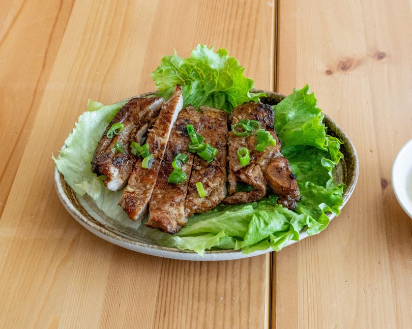 Grilled pork chops, sliced and topped with green onions, served on a bed of lettuce.