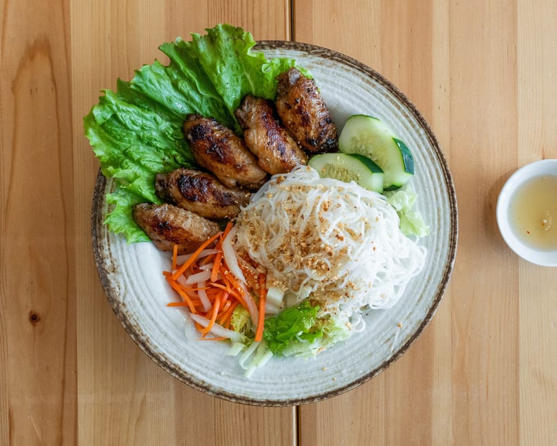 Grilled chicken wings, vermicelli noodles, lettuce, cucumbers, and pickled vegetables on a plate.