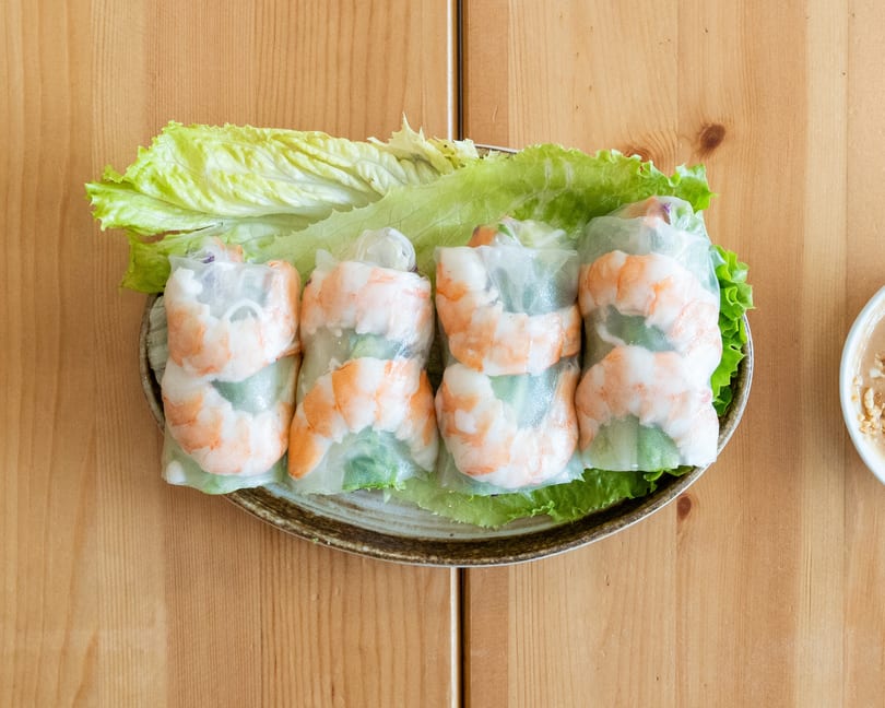 Four fresh shrimp spring rolls on a bed of lettuce, with a side of peanut sauce.